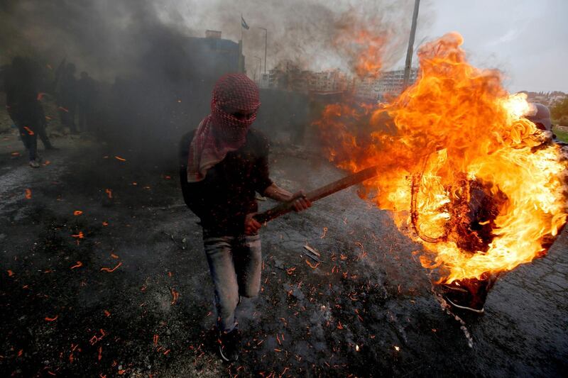 A Palestinian man carries a burning tyre during clashes with Israeli forces. AFP