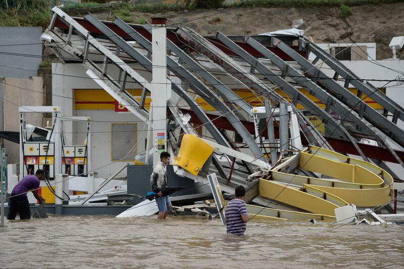 People walk next to a gas station flooded and damaged by the impact of Hurricane Maria, which hit the eastern region of the island, in Humacao, Puerto Rico. Carlos Giusti / AP Photo