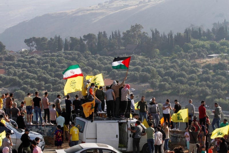 Supporters of Lebanon's Hezbollah lift its flags (C) alongside those of Iran (L) and Palestine, during an anti-Israel protest in the southern Khiam area by the border with Israel, facing the northern Israeli town of Metula, on May 14, 2021. / AFP / Mahmoud ZAYYAT
