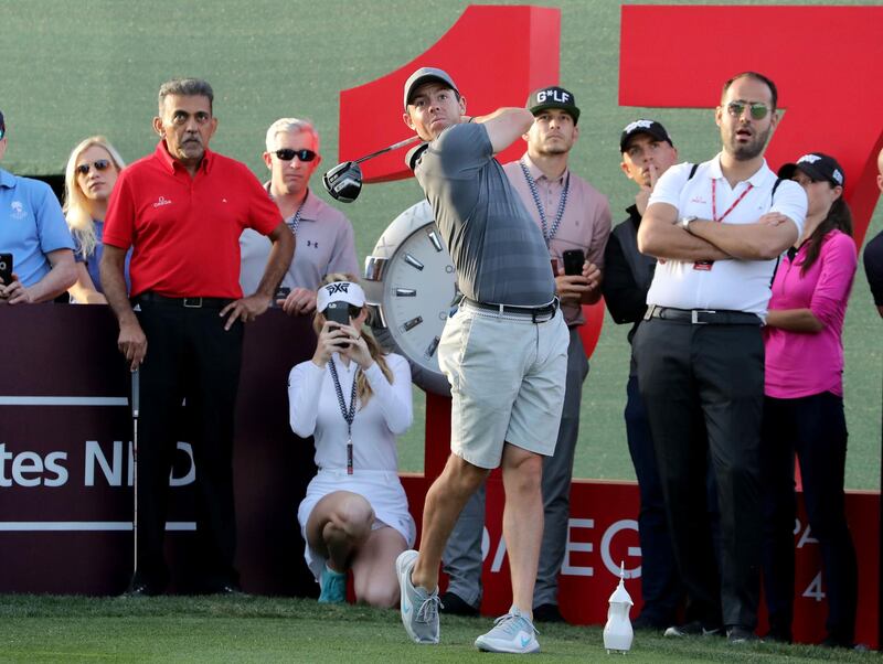 Rory McIlroy plays a shot during the pro-am watched closely by Paige Spiranac (kneeling) at Emirates Golf Club. David Cannon / Getty Images
