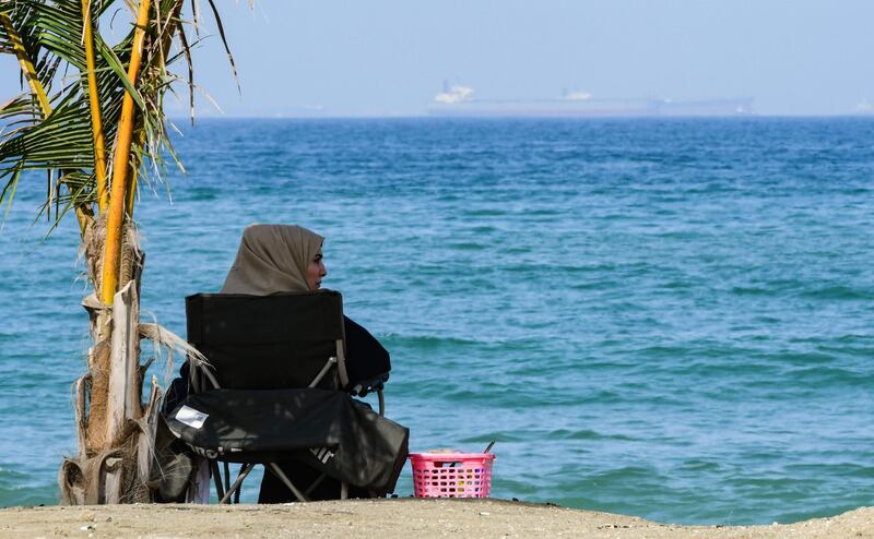 A woman sits along a beach as tanker ships are seen in the waters of the Gulf of Oman off the coast of the eastern UAE emirate of Fujairah on June 15, 2019.  / AFP / GIUSEPPE CACACE
