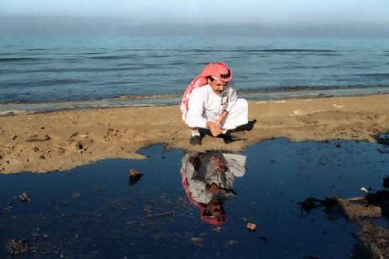 A Saudi journalist bends down to look at a pool of oil on the stained Persian Gulf beach 29 January 1991 near the Kuwait-Saudi border. The United States has sent a team of experts to deal with the threat of several oil spills to the Saudi coastline.