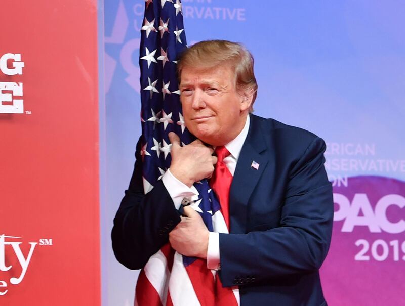 TOPSHOT - US President Donald Trump hugs the US flag as he arrives to speak at the annual Conservative Political Action Conference (CPAC) in National Harbor, Maryland, on March 2, 2019. ALTERNATIVE CROP 
 / AFP / NICHOLAS KAMM / ALTERNATIVE CROP 
