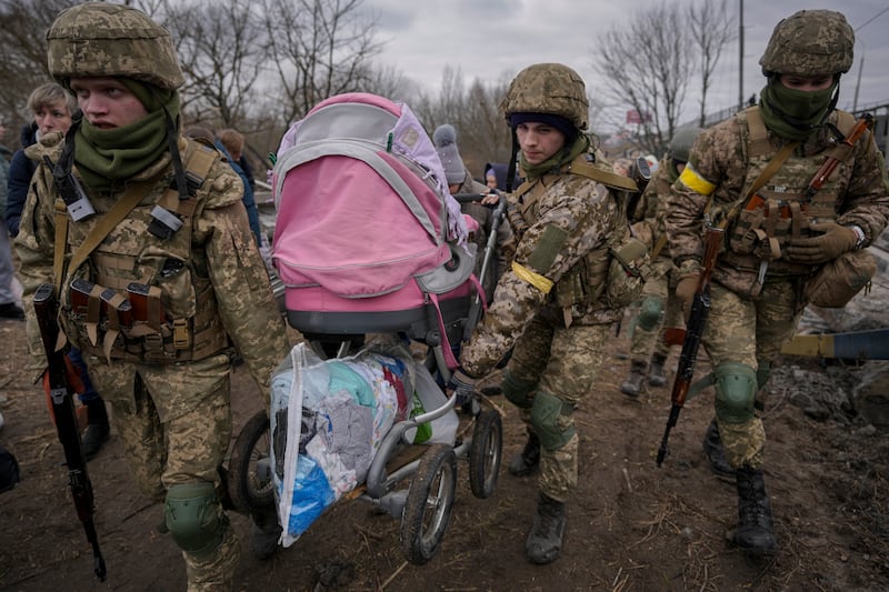 Ukrainian servicemen assist people fleeing the town of Irpin after crossing the Irpin River on an improvised path under a bridge that was destroyed by a Russian air strike. AP Photo