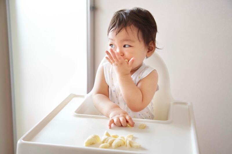 A baby boy eating banana in a high chair. Getty Images