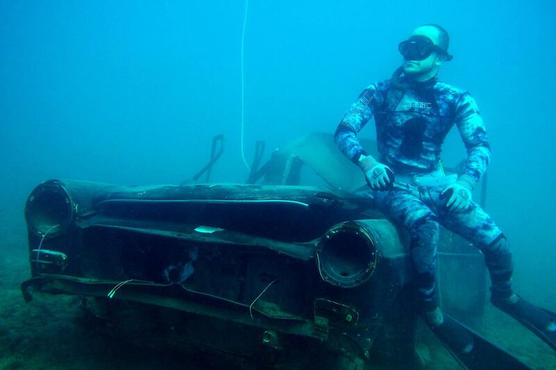 A diver poses next to a sunk car.