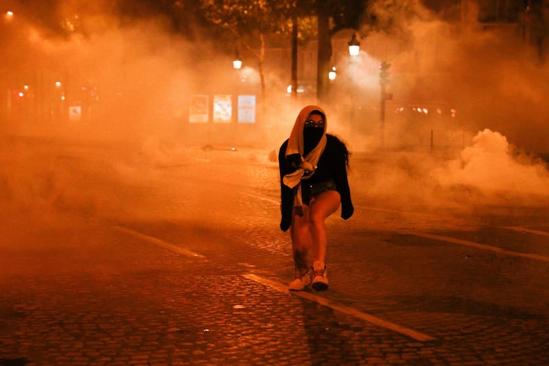 A woman walks covered as PSG supporters flee tear gas canisters on the Champs-Elysees. AFP