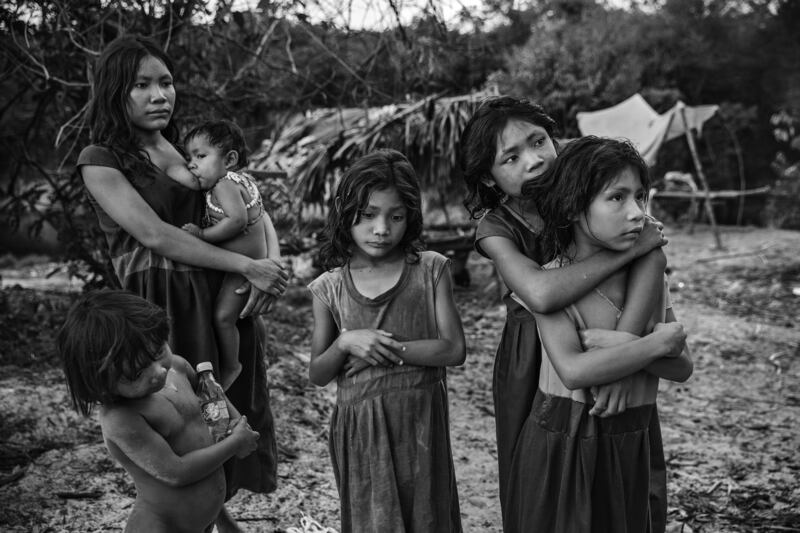 This image provided by World Press Photo, part of a series titled Amazonian Dystopia, by Lalo de Almeida for Folha de Sao Paulo/Panos Pictures which won the World Press Photo Long-Term Project award, shows Women and children from the Piraha community, standing next to their camp on the banks of the Maici River, watch drivers passing by on the Trans-Amazonian highway hoping to be given snacks or soft drinks, Humaita, Amazon, Brazil, Sept.  21, 2016.  (Lalo de Almeida for Folha de Sao Paulo / Panos Pictures / World Press Photo via AP)