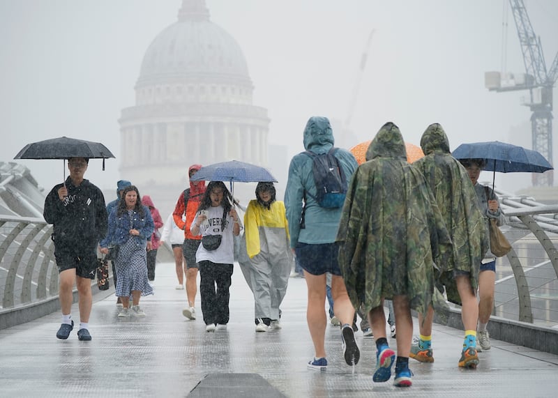 People make their way across the Millennium Bridge during a downpour in London. All photos: PA