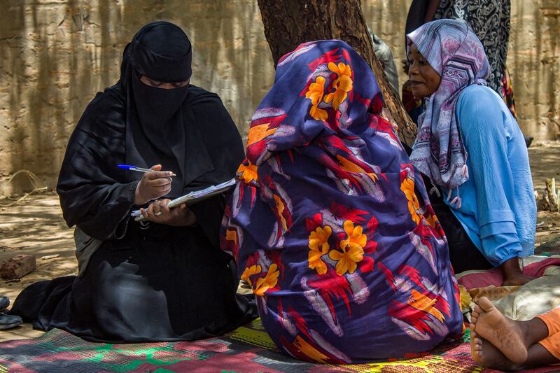 Women are interviewed under the shade of a tree outside at a refugee camp in Al Suwar