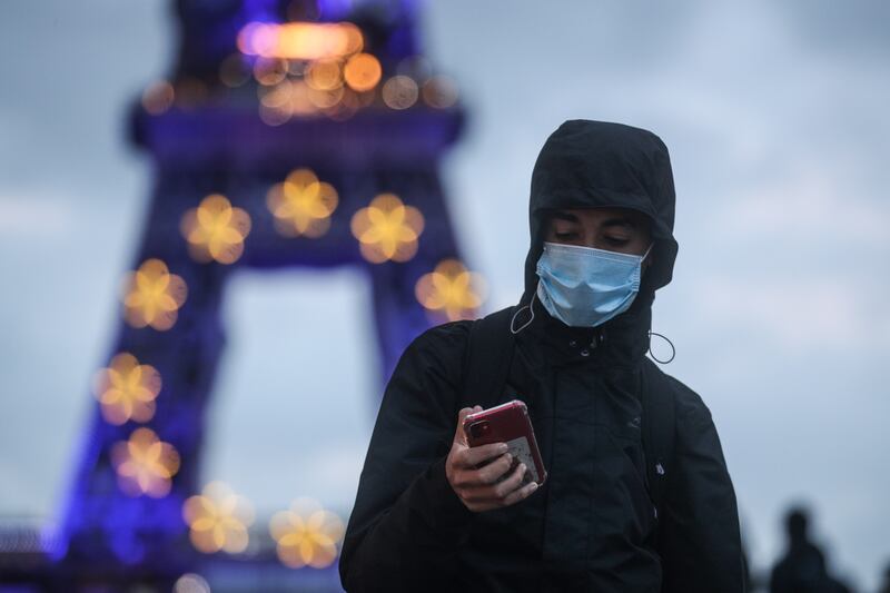 A man wearing a face mask stands next to the Eiffel Tower illuminated in the colors of the EU flag in central Paris, France. EPA