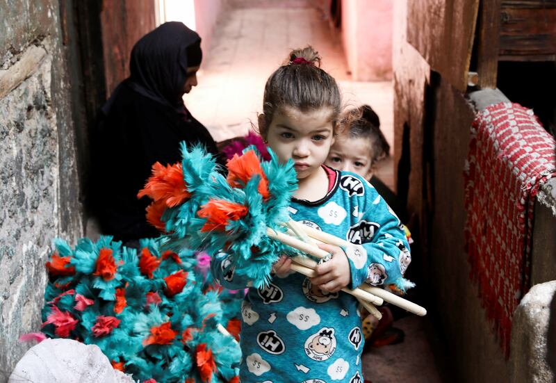 A young girl carries feather dusters made by her grandmother, Saadia Ibrahim, 60, in the background.