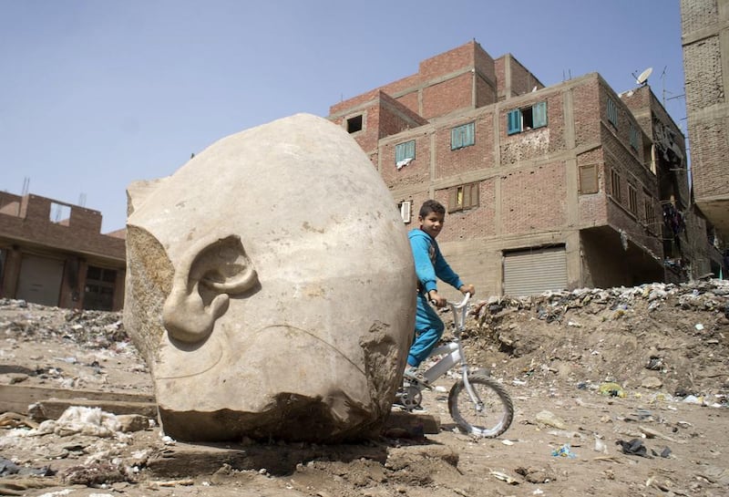 A boy rides his bicycle past the fragment of a recently discovered statue in a Cairo slum that may be of pharaoh Ramses II. Amr Nabil / AP Photo