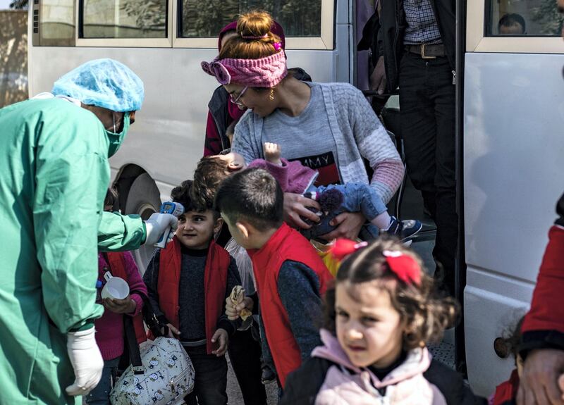 A medic checks the body temperature of young passengers, as a preventive measure against the coronavirus, upon their arrival by bus in Syria's Kurdish area from Iraqi Kurdistan via the Semalka border crossing in northeastern Syria on February 26, 2020. (Photo by Delil SOULEIMAN / AFP)