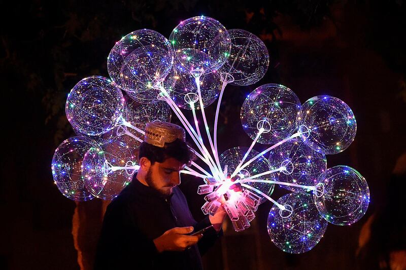 A vendor checks his mobile phone as he sells balloons along a street during a government-imposed nationwide lockdown in Quetta, Pakistan.  AFP