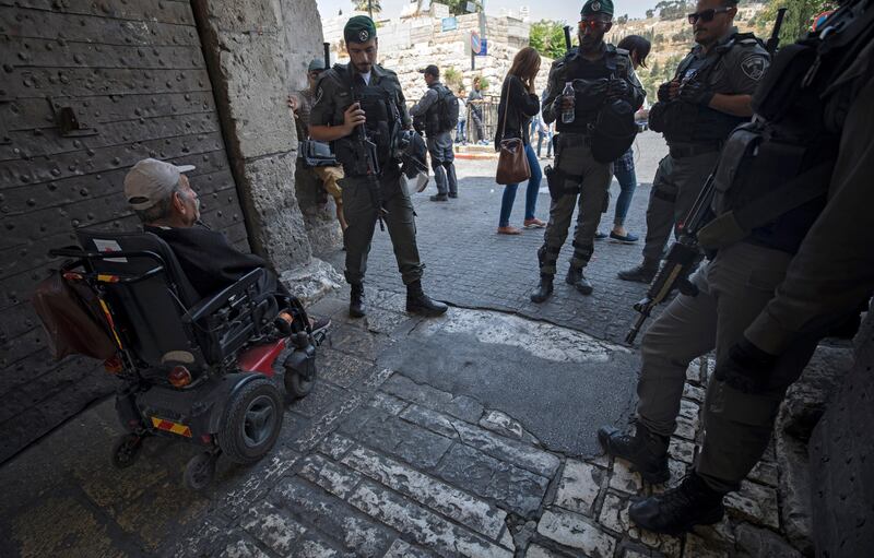 epa06105139 Elderly Palestinian man on wheel chair, passing Israeli security guarding outside Lions' Gate, as part of the security measures taken by the Israeli police in Jerusalem, 23 July 2017. Violent protests are expected to continue after Israeli authorities earlier had installed metal detectors and a new cameras at the entrance to the Al-Aqsa compound after a shooting attack carried out by Israeli Arabs on 14 July against Israeli police during which two Israeli policemen and three attackers were killed. The mufti of Jerusalem had called Palestinian Muslims not to go through the electronic gates and to reject all procedures that change the historic situation of the mosque. The measures reportedly were prohibiting Friday prayers for Muslims at the mosque for the first time in 48 years.  EPA/ATEF SAFADI