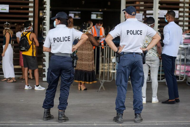 Police offciers stand guard as travellers wearing protective face masks queue for check-in on an Air Austral flight to Paris, from Dzaoudzi Airport in Petite Terre on the French Indian Ocean island of Mayotte, as measures to curb the spread of the COVID-19 (novel coronavirus) are maintained on Mayotte over concerns about the continued spread of the virus there and a fragile health system.  AFP