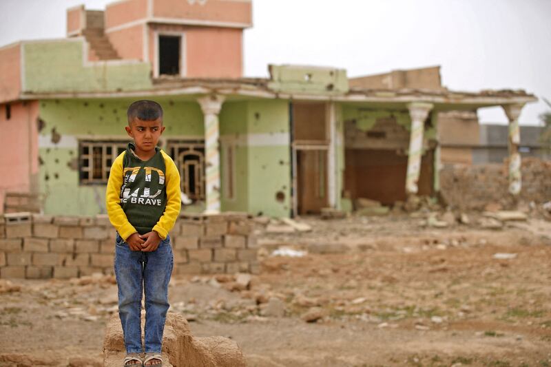 A boy stands by a destroyed house.