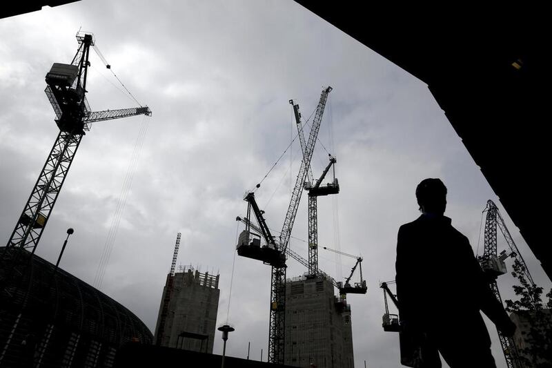 A pedestrian walks past construction cranes as they work above a building site in London. UK GDP rose 0.9 per cent in the first quarter, up from 0.7 per cent in the final three months of 2013, according to the median of estimate in a Bloomberg News survey of economists. Simon Dawson / Bloomberg