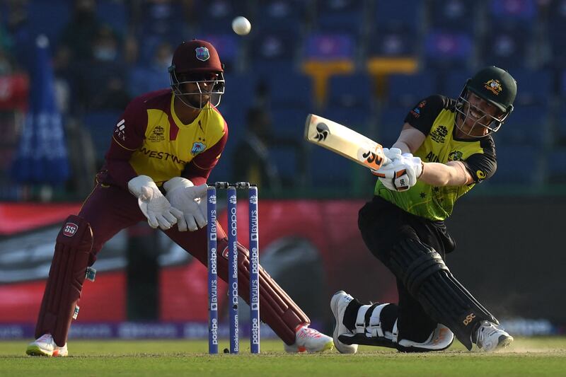 Australia's David Warner (R) plays a shot as West Indies' wicketkeeper Nicholas Pooran watches during the ICC men’s Twenty20 World Cup cricket match between Australia and West Indies at the Sheikh Zayed Cricket Stadium in Abu Dhabi on November 6, 2021.  (Photo by INDRANIL MUKHERJEE  /  AFP)