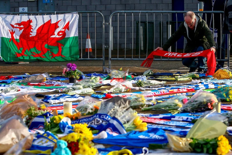 A man adds a Wales scarf to the display of Cardiff City scarves and jerseys, flowers, messages and other tributes to the football club's new signing Emiliano Sala, whose flight disappeared from radar over the English Channel north of Guernsey, placed outside the Cardiff City Stadium in Cardiff, south Wales on January 25, 2019.  British investigators said on January 25 they were probing the licence held by the pilot of the small plane carrying Premier League player Emiliano Sala that went missing over the Channel this week. Police on January 24 ended their search for Sala, saying the chances of finding the Argentinian alive three days after his small plane went missing were "extremely remote". The light aircraft transporting the 28-year-old striker, who signed for Cardiff City at the weekend, disappeared from radar around 20 kilometres (12 miles) north of Guernsey on the night of January 21.
 / AFP / GEOFF CADDICK
