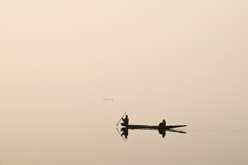 A man steers a boat across Dal Lake on a foggy day in Srinagar on December 12, 2023.  (Photo by TAUSEEF MUSTAFA  /  AFP)
