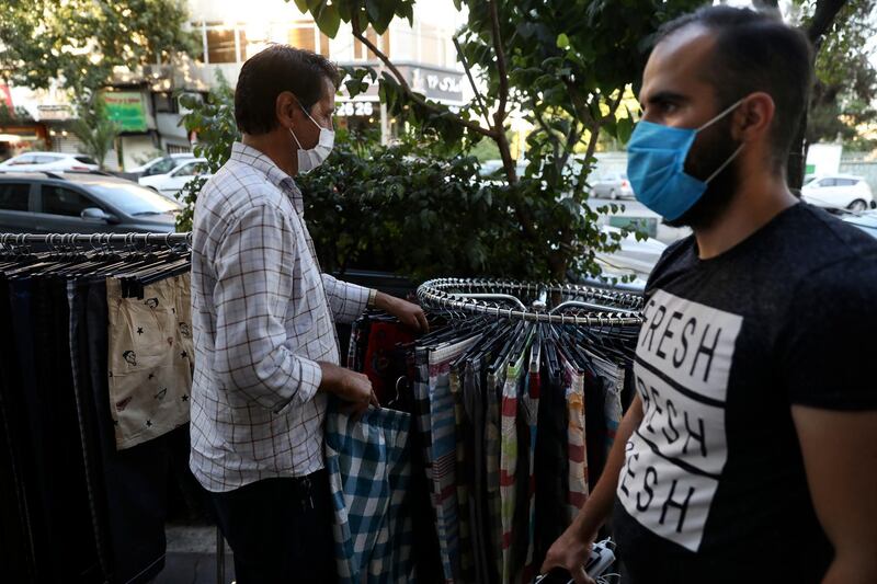 A vendor wearing a protective face mask to help prevent the spread of the coronavirus adjusts his items as a pedestrian walks past on a commercial street in Tehran, Iran, Wednesday, July 15, 2020. Iran's President Hassan Rouhani has said lockdowns over COVID-19 pandemic may lead to street protests over economic problems, though in Tehran, authorities have decided to impose some restrictions again over newly spiking reported deaths from the coronavirus. (AP Photo/Vahid Salemi)