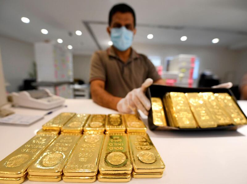 A jeweller, wearing a face mask and latex gloves due to the COVID-19 coronavirus pandemic, showcases bars of gold at a shop at the Dubai Gold Souk in the Gulf emirate on May 13, 2020, as markets re-open amidst an easing of pandemic restrictions. Evening dresses made of gold mesh, gilded sunglasses and glittering crowns are sparkling again from the windows of Dubai’s historic gold souk which was shuttered during the coronavirus lockdown. Though customers are still missing, for business owners, the reopening of one of the world’s biggest gold markets is a vital move towards normality ahead of the autumn tourist season, in a city that prides itself on shop-'til-you-drop experiences. / AFP / Karim SAHIB
