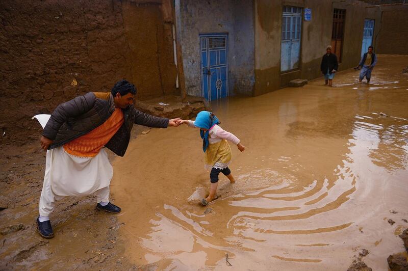 An Afghan man helps a girl as she wades along a street affected by flash floods in Herat province. AFP