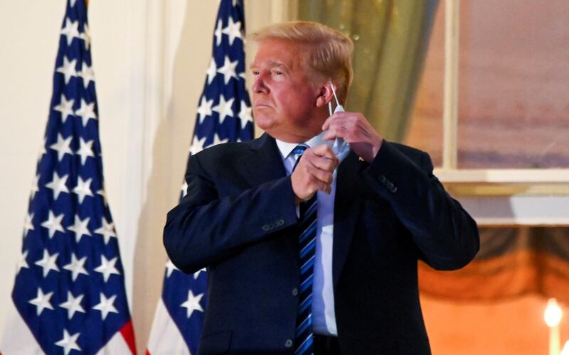 US President Donald Trump pulls off his protective face mask as he poses atop the Truman Balcony of the White House after returning from being hospitalized at Walter Reed Medical Center for Covid-19 treatment, on October 5, 2020. Reuters