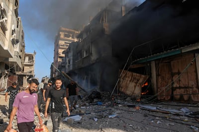 Palestinians walk amid the rubble and smoke of a building hit in an Israeli air strike on October 13. AFP