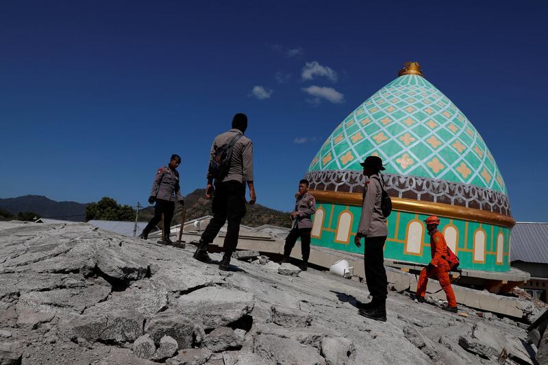 Rescuers and policemen walk on top of a collapsed mosque. Reuters