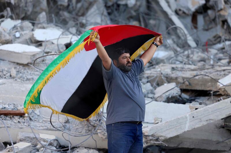 A Palestinian lifts a national flag in front of a building destroyed by Israeli air strikes in Gaza City. AFP