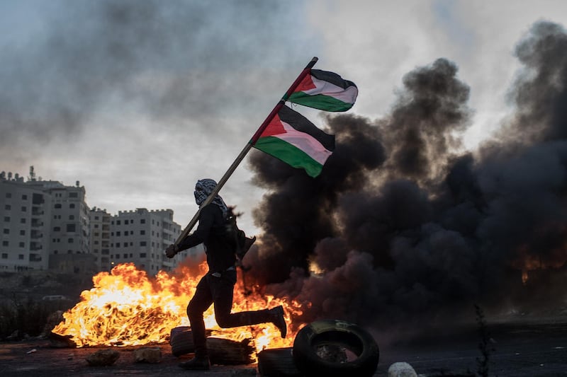 A Palestinian protester runs past a burning barricade carrying a Palestinian flag during clashes with Israeli border guards near an Israeli checkpoint in Ramallah, West Bank. Chris McGrath/ Getty Images