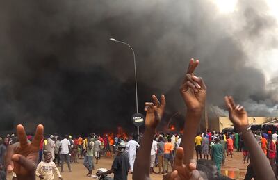 With the headquarters of the ruling party burning in the background, supporters of mutinous soldiers demonstrate in Niamey, Niger. AP 