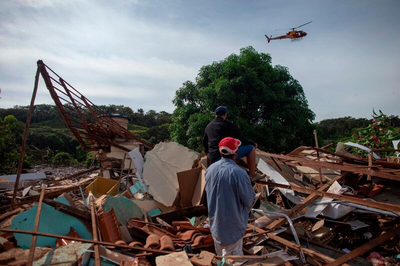 People from the community of Parque da Cachoeira look at a firefighter helicopter flying over the mud-hit area a day after the collapse of a dam at an iron-ore mine belonging to Brazil's giant mining company Vale near the town of Brumadinho in the state of Minas Gerias in southeastern Brazil  AFPl