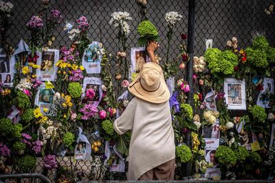 A woman adds flowers to a memorial featuring photos of some of those lost in the partially collapsed 12-story Champlain Towers South building on June 28, 2021 in Surfside, Florida. Questions mounted Monday about how a residential building in the Miami area could have collapsed so quickly and violently last week, as the death toll rose to 11 with 150 still unaccounted for, and desperate families feared the worst. / AFP / Giorgio Viera
