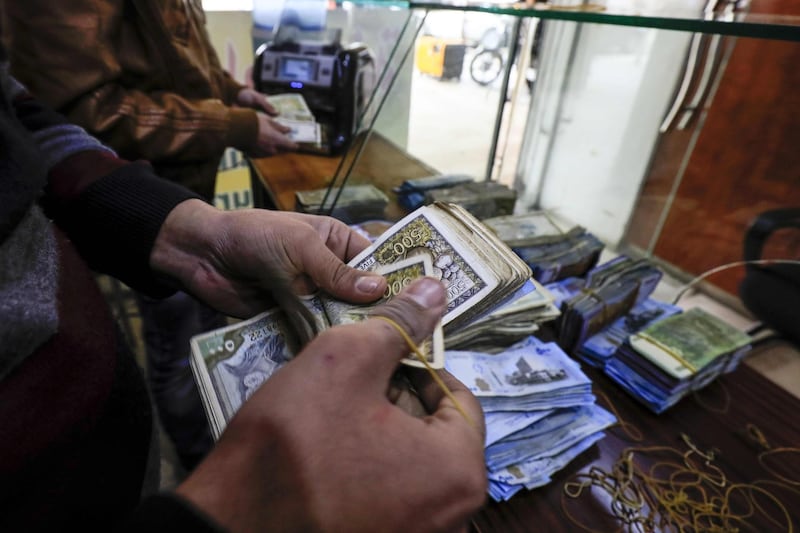 An employee of a currency exchange counter counts banknotes at a market street in the northeastern Syrian town of Qamishli on May 2, 2018.  Many Kurds in Syria may dream of self-rule, but for business owners in the semi-autonomous region in the country's north, it now comes with a painful pinch: double taxes paid both to Kurdish authorities and the central government in Damascus.  / AFP / Delil souleiman
