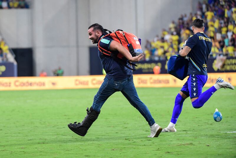 An emergency service member runs on the pitch carrying medical equipment during a play interruption after a supporter collapsed in the stands. AFP