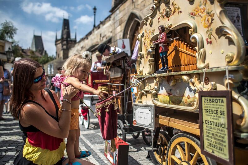 epa06131978 A girl give coins into a money box placed on a barrel organ at the 4th International Organ Grindes Festival under the Charles Bridge in Prague, Czech Republic, 08 August 2017. The Czech National Museum hosts an one-day gathering of barrel organ players from Czech Republic, Poland, Germany, Austria, Slovakia and Switzerland. The barrel organ, also known as a roller organ, has been played on the streets of Europe since the 18th century.  EPA/MARTIN DIVISEK