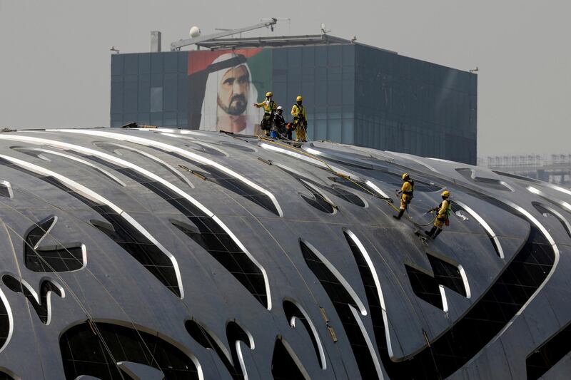 Workers clean the fascade of The Museum of the Future within sight of a portrait of Prime Minister and Vice-President of the United Arab Emirates and ruler of Dubai Sheikh Mohammed bin Rashid al-Maktoum in Dubai, United Arab Emirates, June 9, 2021. Picture taken June 9, 2021. REUTERS/Christopher Pike