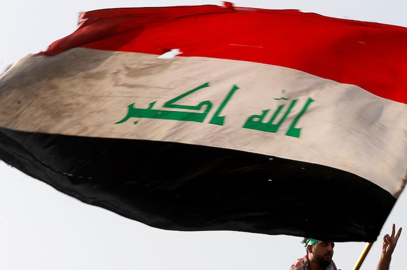 A demonstrator holds an Iraqi flag as another gestures while they gather to mark the first anniversary of the anti-government protests in Baghdad. Reuters