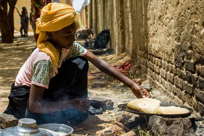 A girl prepares food outside at a camp for the internally displaced in Al Suwar