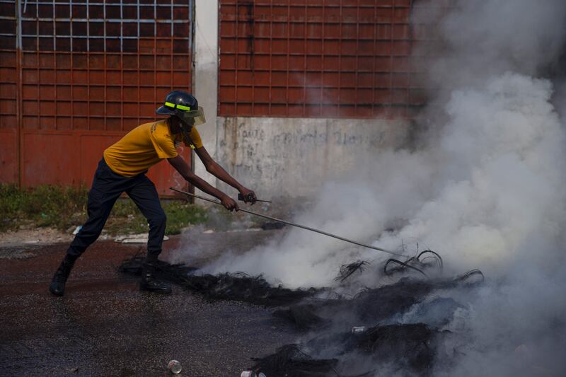 A firefighter puts out a smoldering road block set up by protesters in Port-au-Prince. AP