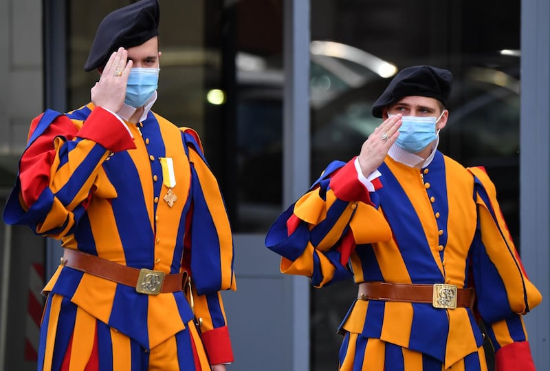 Swiss Guards wearing a face mask give a salute as they stand guard at an entrance of The Vatican.  AFP