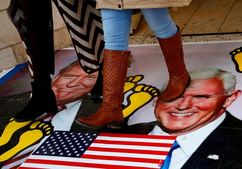 Palestinians walk on a poster bearing images of US President Donald Trump (L) and his deputy Mike Pence during a demonstration at the al-Quds Open University in Dura village on the outskirts of the West Bank town of Hebron on December 13, 2017, as protests continue in the region amid anger over US President Donald Trump's recognition of Jerusalem as its capital.  / AFP PHOTO / HAZEM BADER