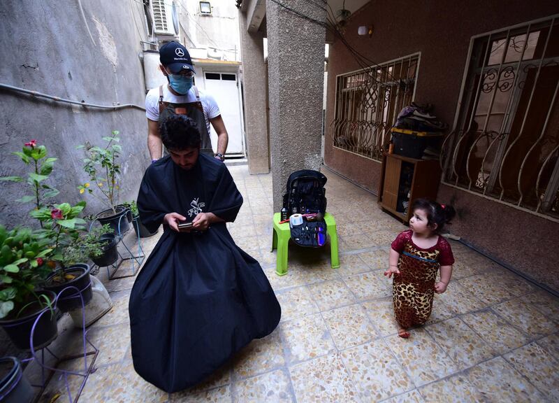 Iraqi itinerant barber Hussain Majid  wears a face mask as he gives a haircut to a client at his house in Baghdad.  EPA