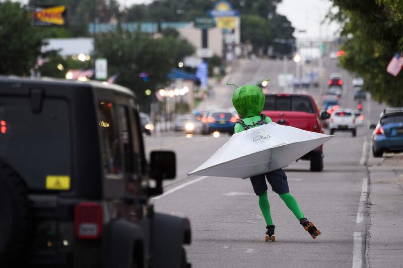 A person wearing an alien costume roller skates through traffic down Main Street during the UFO Festival. AFP