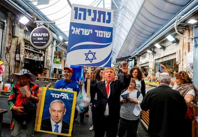 TOPSHOT - A supporter of Israeli Prime Minister Benjamin Netanyahu wearing a mask with the face of US President Donald Trump marches with a sign reading in Hebrew "guardian of Israel" and a Likud Party electoral portrait of Netanyahu along an alley of the Machane Yehuda market in Jerusalem on April 7, 2019, while campaigning for Netanyahu two days ahead of the electoral polls.  / AFP / MENAHEM KAHANA
