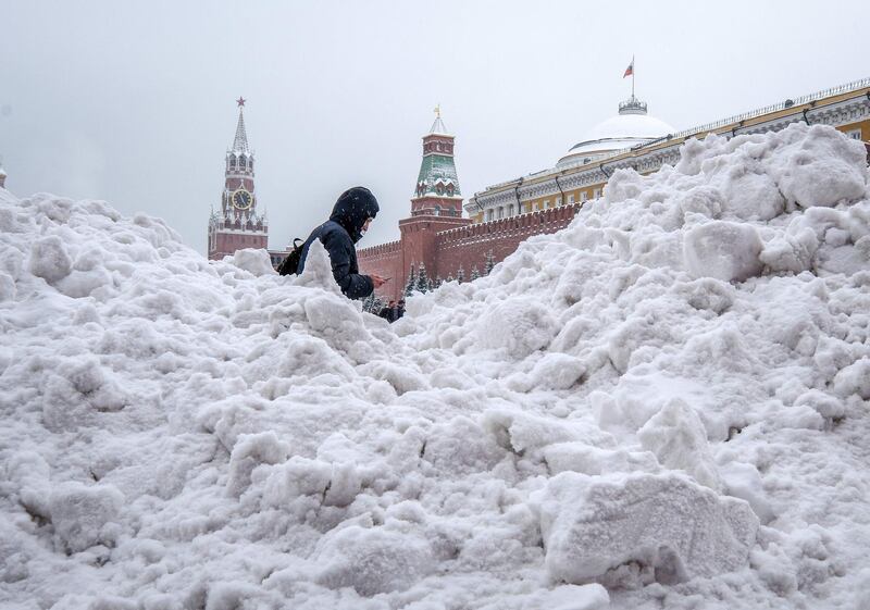 A man uses his mobile phone as he passes a snow heap at Red Square, with the Kremlin seen in the background, after a night of heavy snowfall in Moscow. AFP
